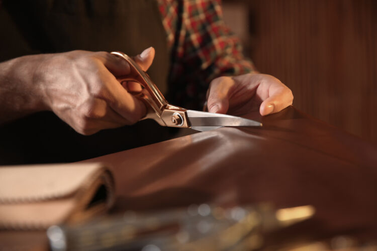 man cutting leather with scissors in workshop, closeup